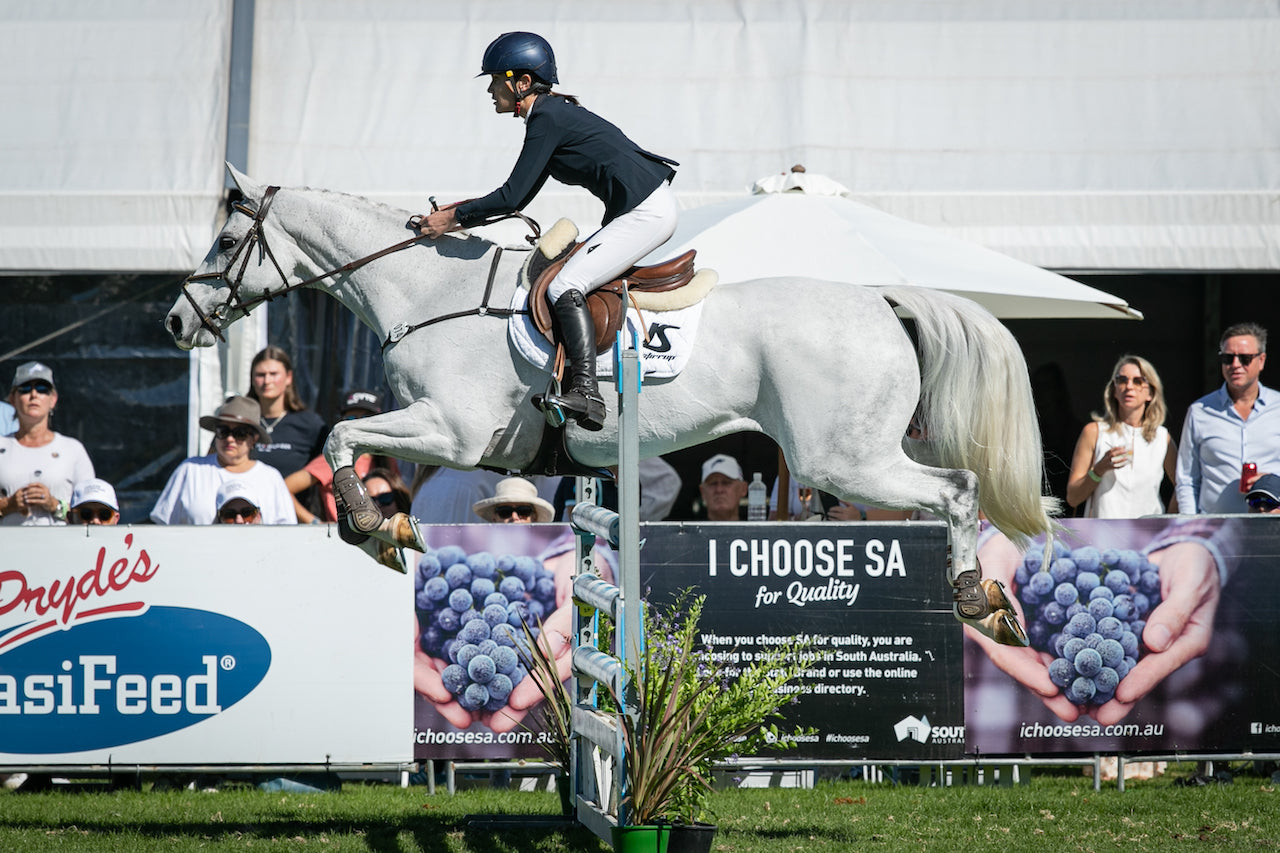 Girl riding white horse jumping over hurdle with jinstirrup equipment 